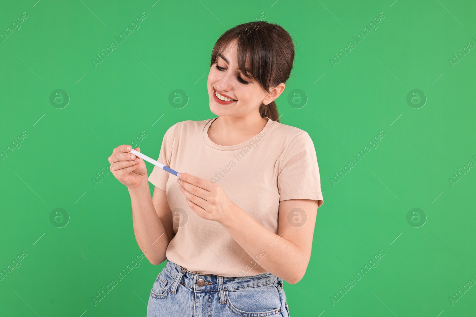 Photo of Happy young woman with pregnancy test on green background