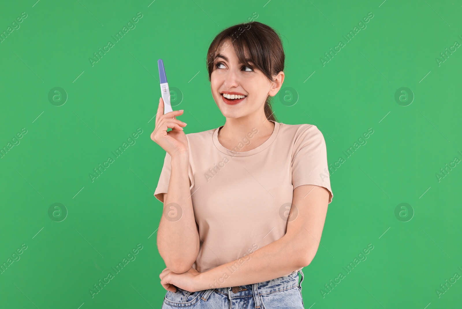 Photo of Happy young woman with pregnancy test on green background