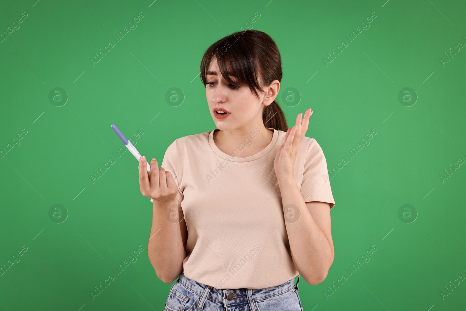 Photo of Worried young woman with pregnancy test on green background