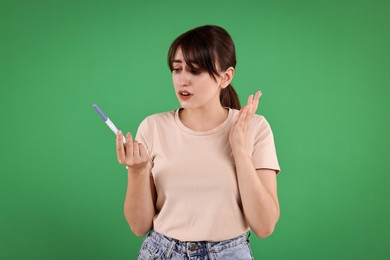 Worried young woman with pregnancy test on green background