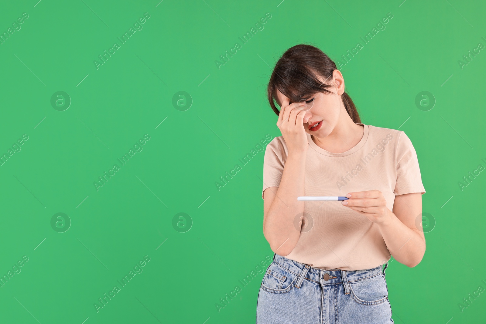 Photo of Worried young woman with pregnancy test on green background, space for text