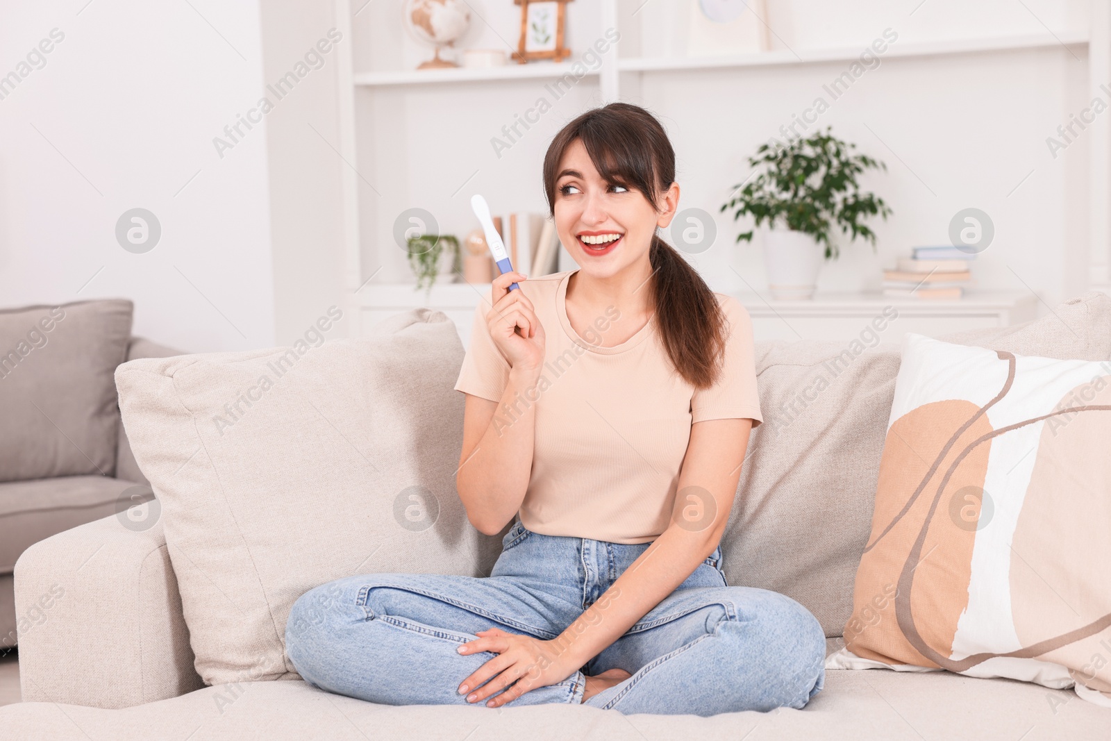 Photo of Happy young woman with pregnancy test on sofa at home