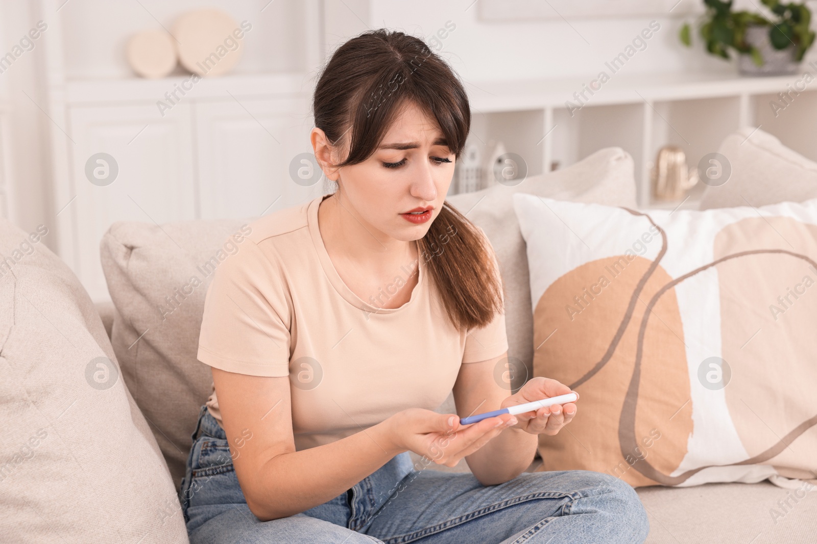 Photo of Worried young woman with pregnancy test on sofa at home