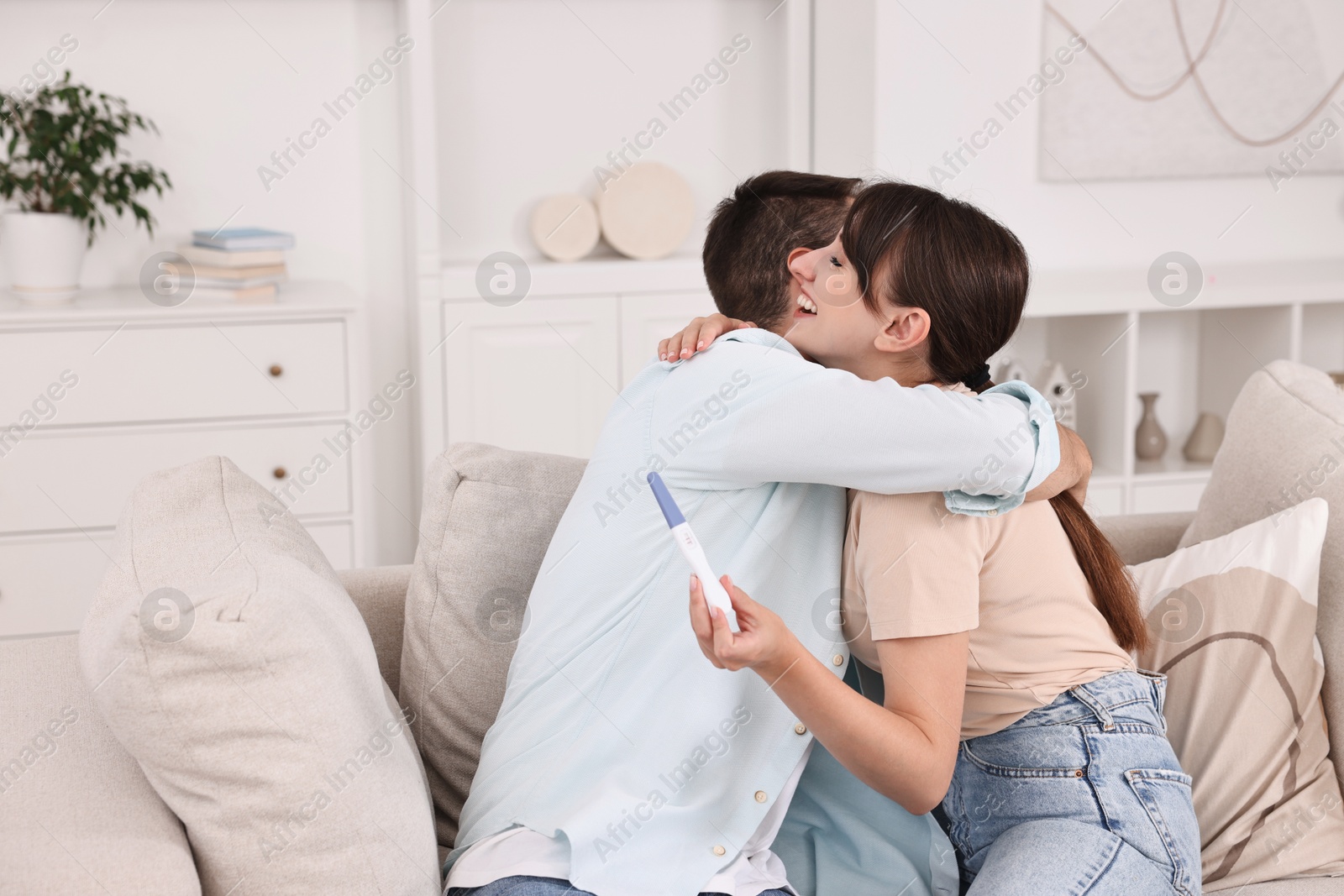 Photo of Happy young couple with pregnancy test on sofa at home