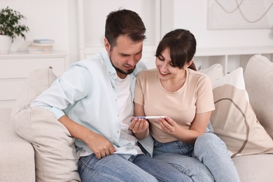 Happy young couple with pregnancy test on sofa at home