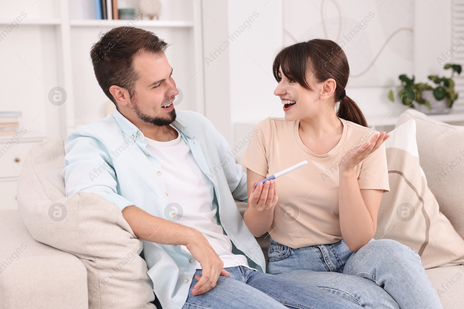 Photo of Happy young couple with pregnancy test on sofa at home