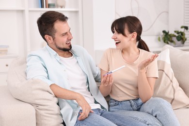 Happy young couple with pregnancy test on sofa at home