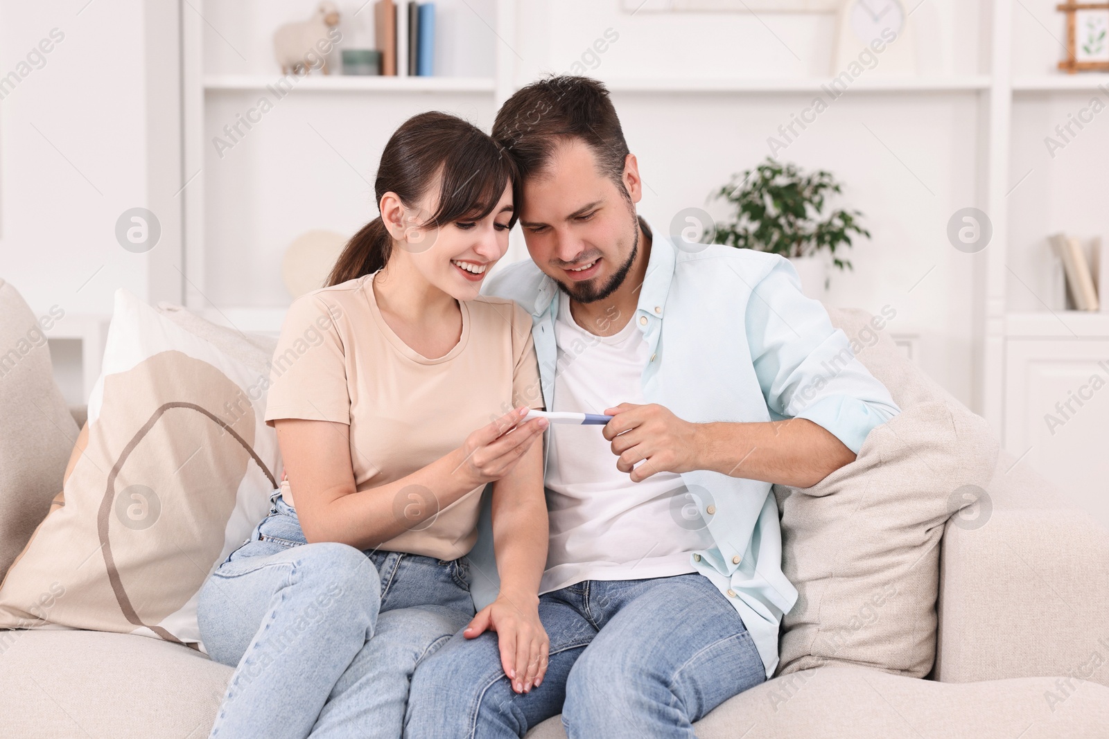 Photo of Happy young couple with pregnancy test on sofa at home