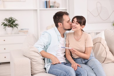 Photo of Happy young couple with pregnancy test on sofa at home