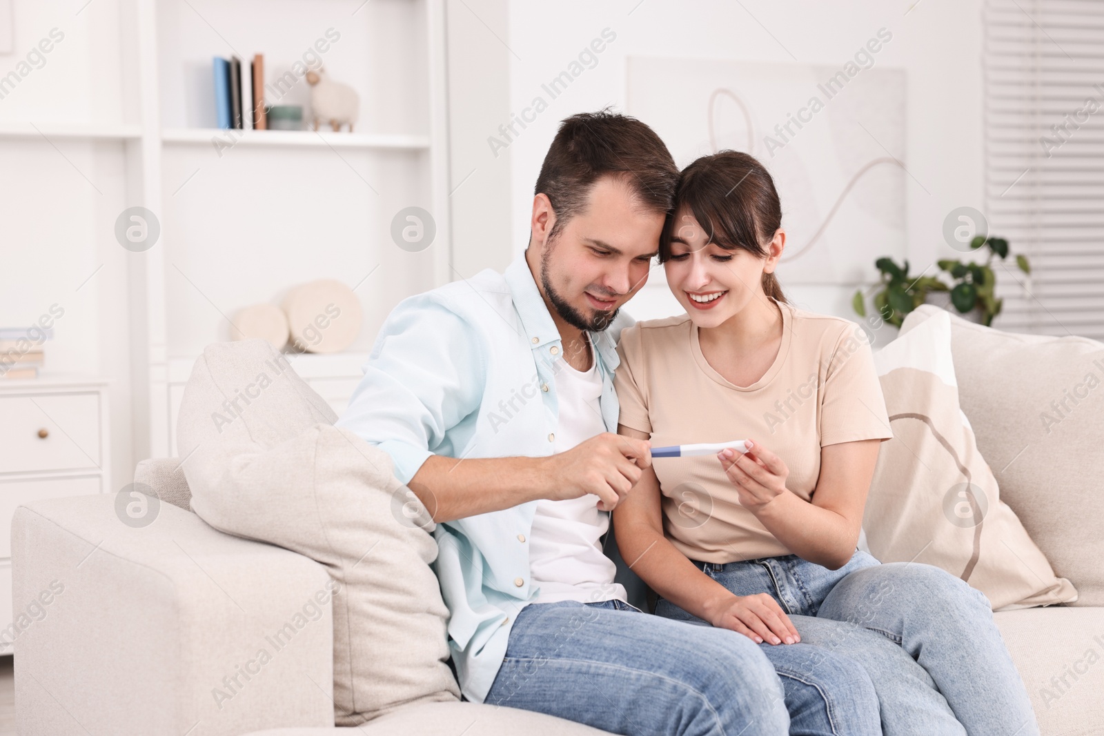 Photo of Happy young couple with pregnancy test on sofa at home