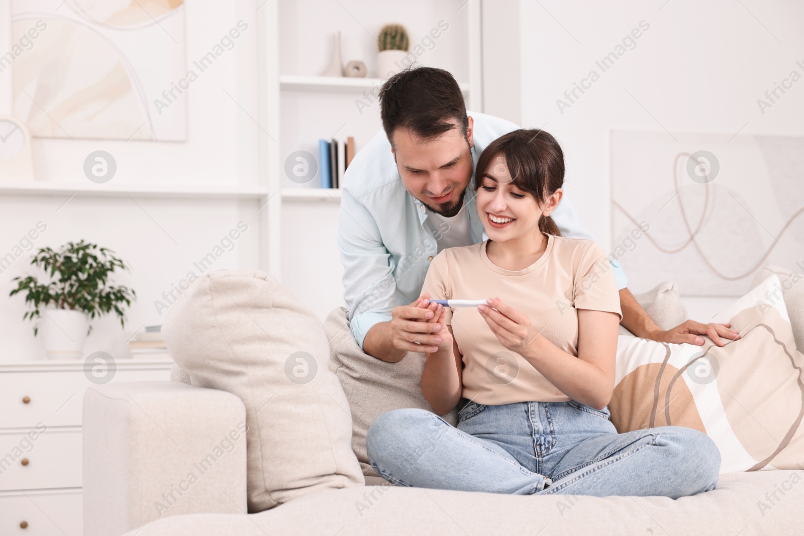 Photo of Happy young couple with pregnancy test on sofa at home