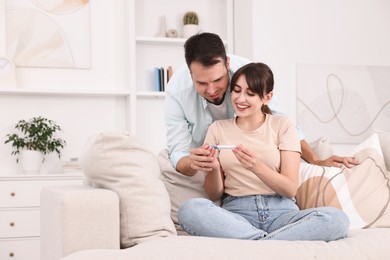 Photo of Happy young couple with pregnancy test on sofa at home