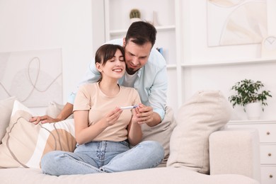 Photo of Happy young couple with pregnancy test on sofa at home