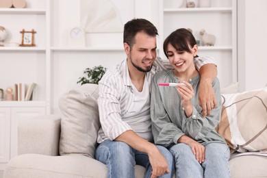 Happy young couple with pregnancy test on sofa at home, space for text