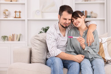 Happy young couple with pregnancy test on sofa at home, space for text