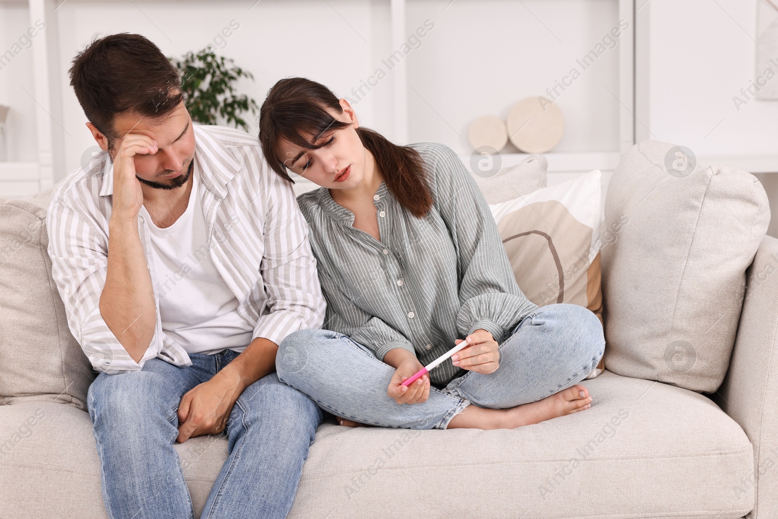 Photo of Worried young couple with pregnancy test on sofa at home