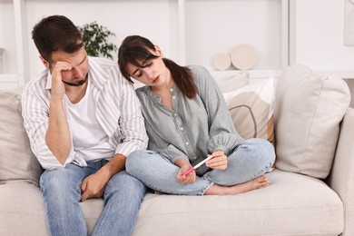 Photo of Worried young couple with pregnancy test on sofa at home