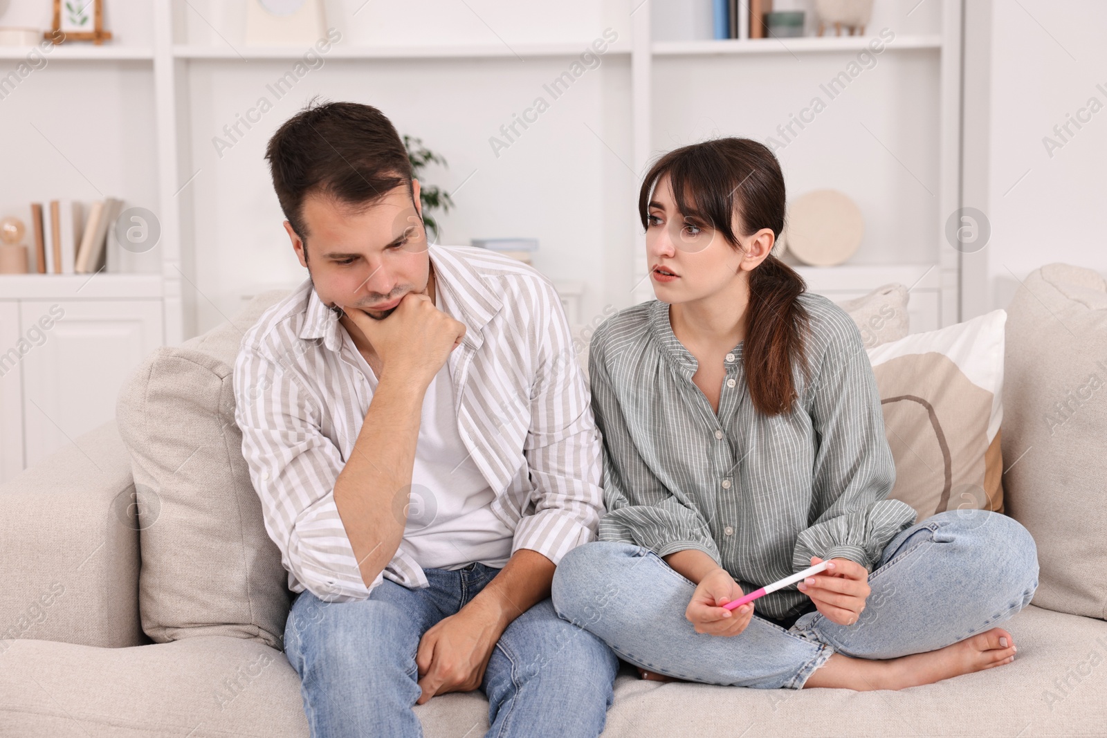 Photo of Worried young couple with pregnancy test on sofa at home