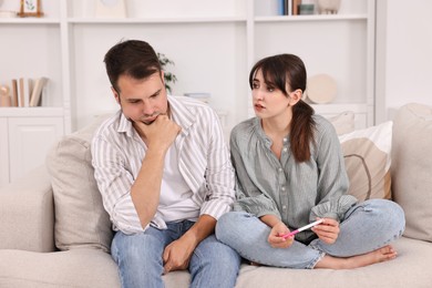 Worried young couple with pregnancy test on sofa at home