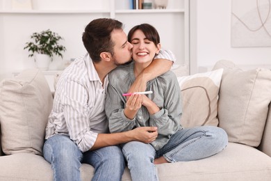 Photo of Happy young couple with pregnancy test on sofa at home