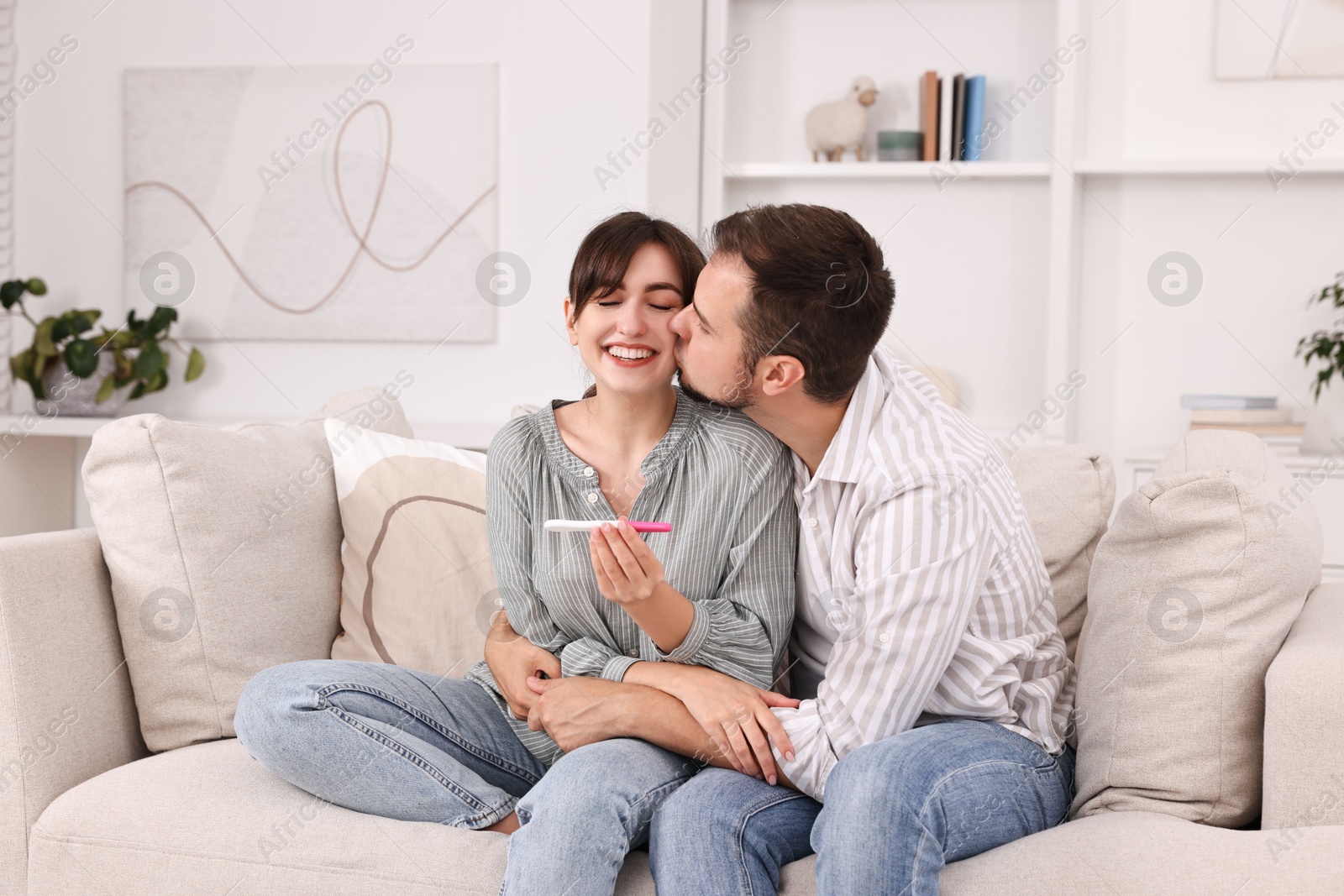 Photo of Happy young couple with pregnancy test on sofa at home