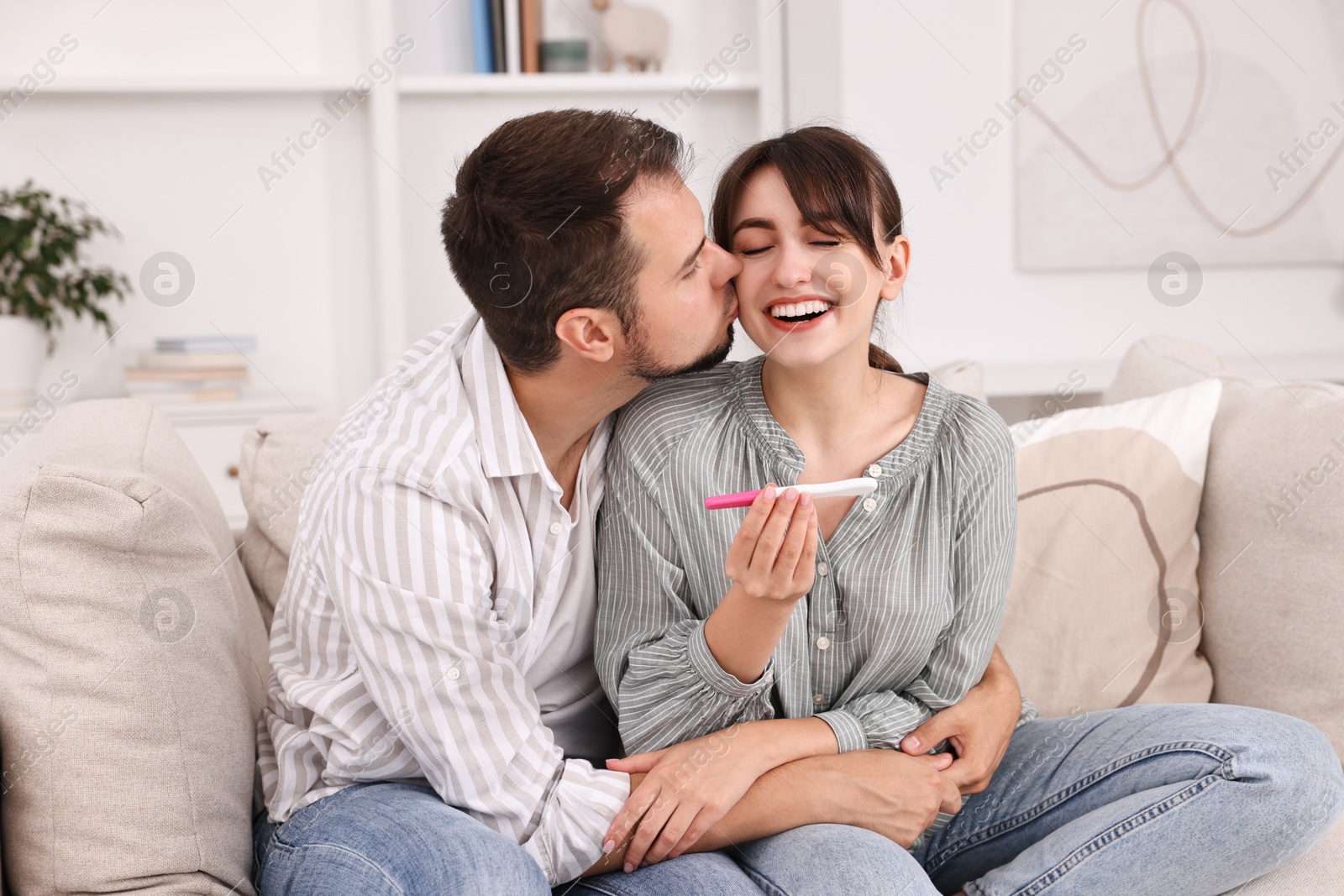 Photo of Happy young couple with pregnancy test on sofa at home