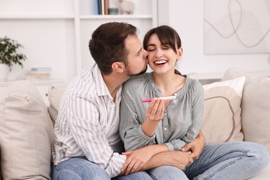 Happy young couple with pregnancy test on sofa at home