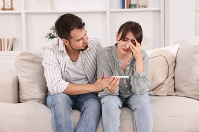 Photo of Worried young couple with pregnancy test on sofa at home