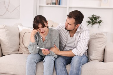 Photo of Worried young couple with pregnancy test on sofa at home