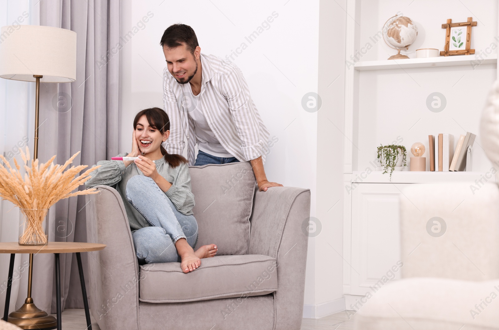 Photo of Happy young couple with pregnancy test at home, space for text