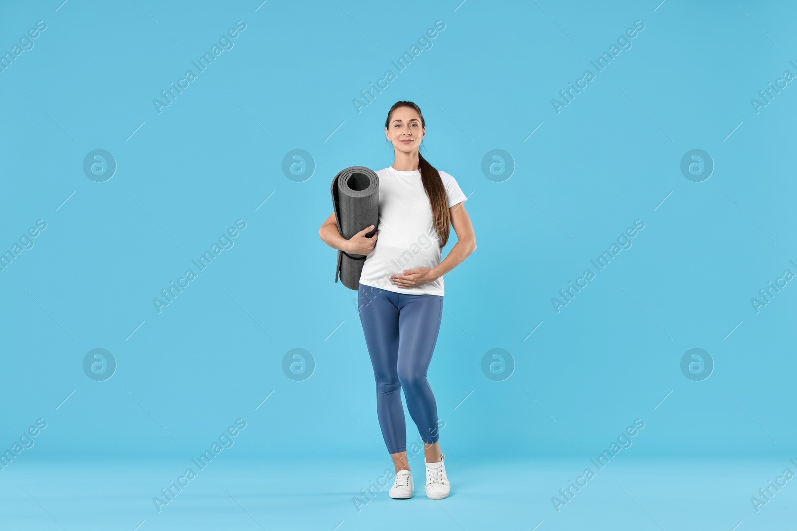 Photo of Beautiful pregnant woman with exercise mat on light blue background