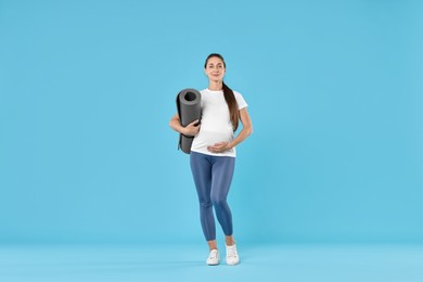 Beautiful pregnant woman with exercise mat on light blue background