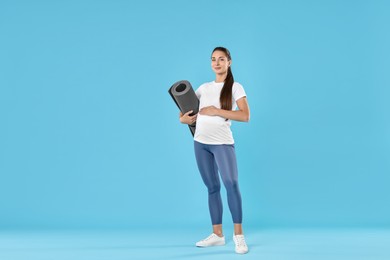 Beautiful pregnant woman with exercise mat on light blue background