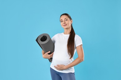 Beautiful pregnant woman with exercise mat on light blue background