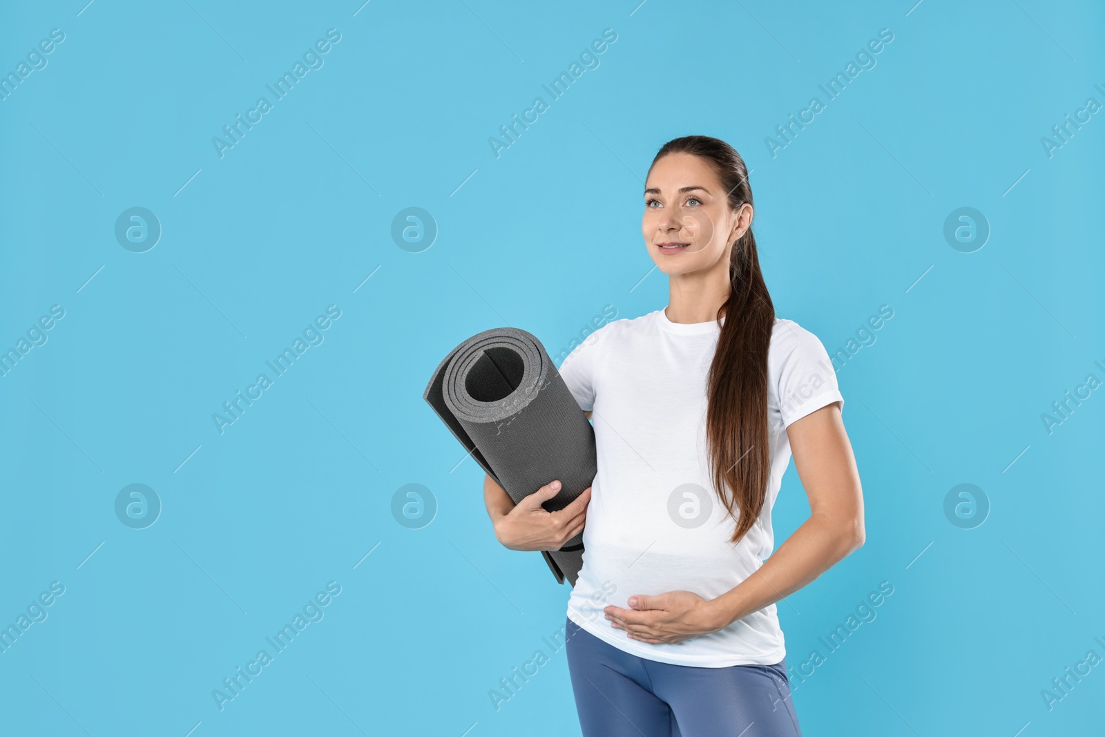 Photo of Beautiful pregnant woman with exercise mat on light blue background