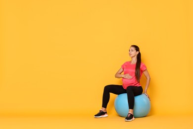 Photo of Beautiful pregnant woman doing exercises on fitball against yellow background, space for text