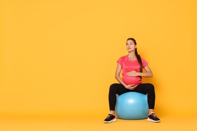 Beautiful pregnant woman doing exercises on fitball against yellow background, space for text