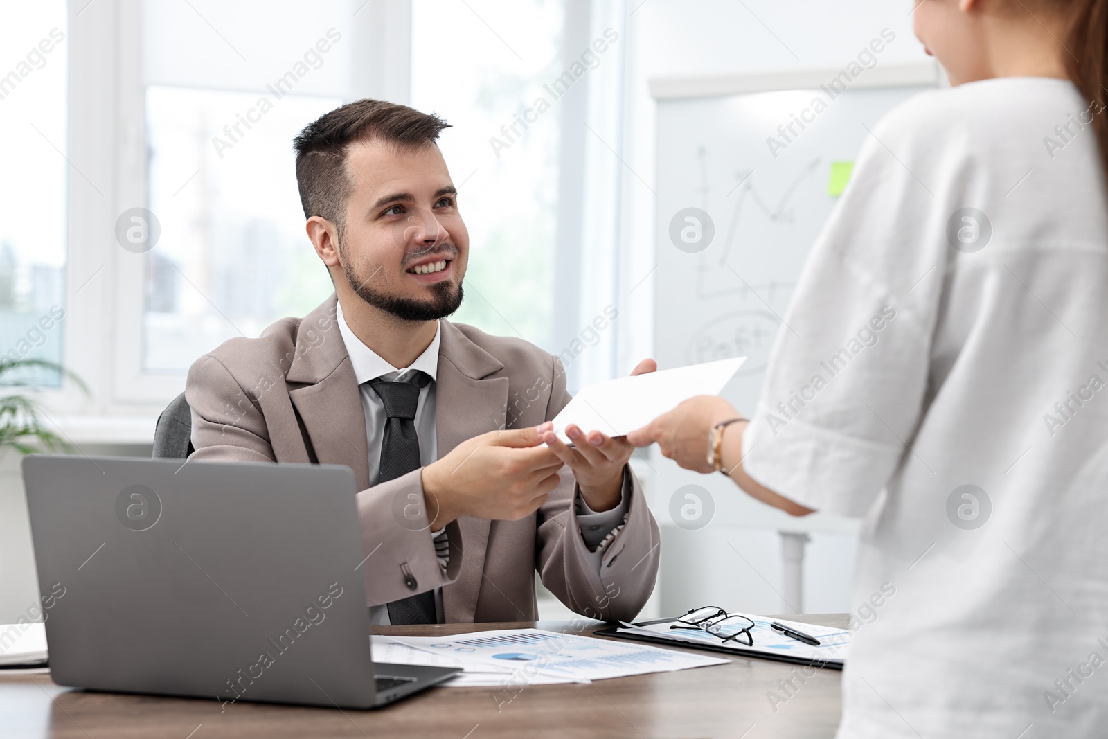 Photo of Smiling employee receiving envelope with salary from boss in office