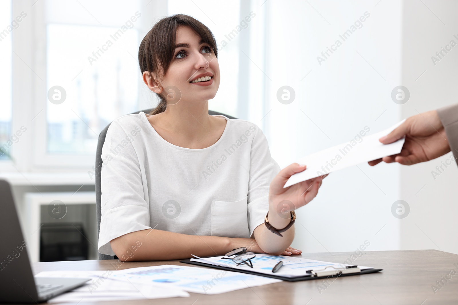 Photo of Smiling employee receiving envelope with salary from boss in office