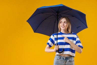 Photo of Woman with blue umbrella pointing at something on yellow background