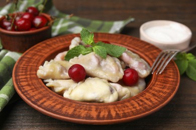 Photo of Traditional Ukrainian dumplings (varenyky) with cherries served on wooden table, closeup