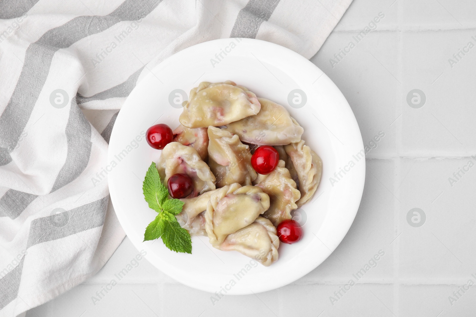 Photo of Traditional Ukrainian dumplings (varenyky) with cherries on white tiled table, top view