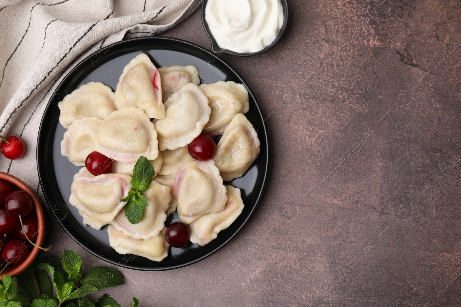 Photo of Traditional Ukrainian dumplings (varenyky) with cherries served on brown table, flat lay. Space for text