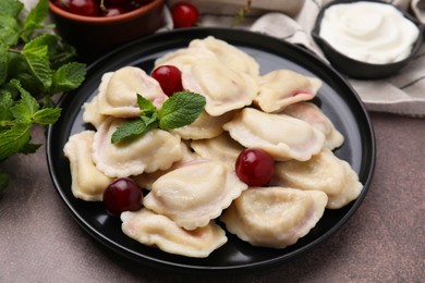 Photo of Traditional Ukrainian dumplings (varenyky) with cherries served on brown table, closeup