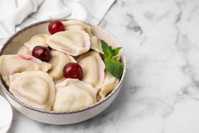 Traditional Ukrainian dumplings (varenyky) with cherries served on white marble table, closeup. Space for text