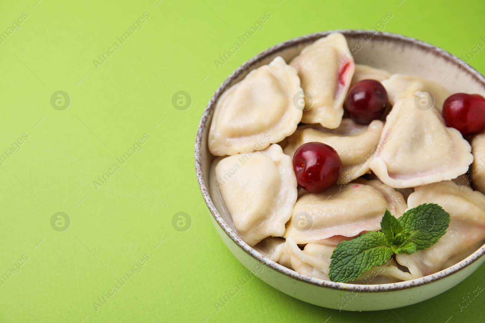 Photo of Traditional Ukrainian dumplings (varenyky) with cherries on green background, closeup. Space for text