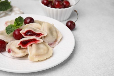 Photo of Traditional Ukrainian dumplings (varenyky) with cherries served on light table, closeup