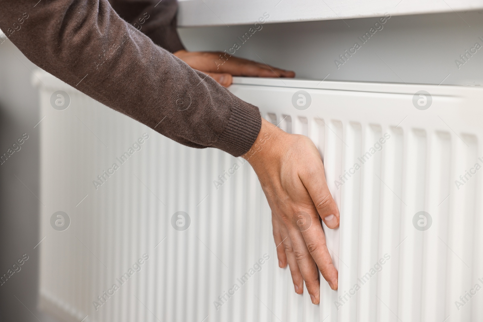 Photo of Man warming hands near heating radiator indoors, closeup