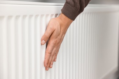 Photo of Man warming hand near heating radiator indoors, closeup