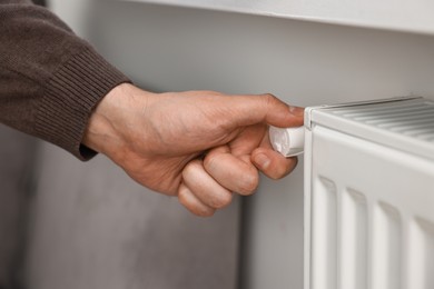 Photo of Man adjusting temperature of heating radiator indoors, closeup